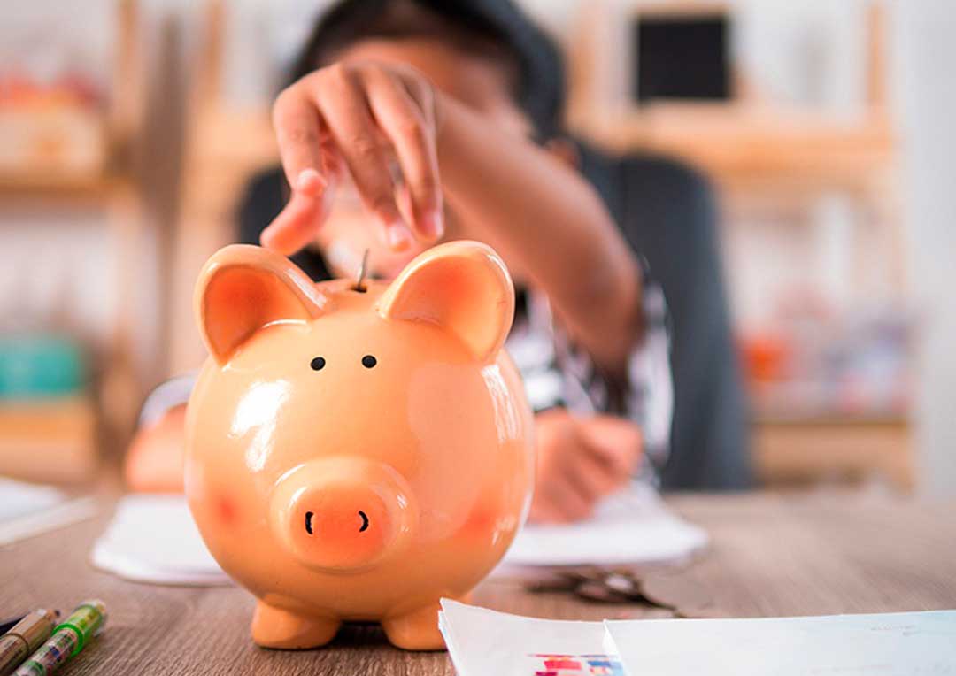 criança colocando moeda em cofrinho em formato de porquinho