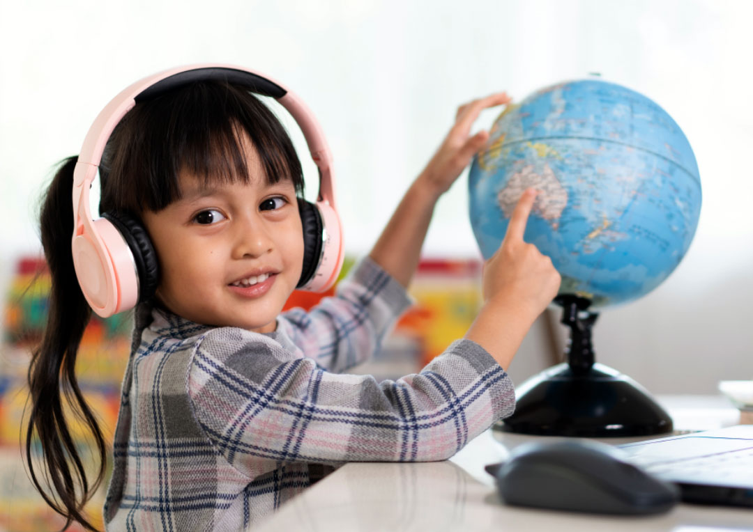 criança sorringo usando fone de ouvindo e apontando para um globo terrestre