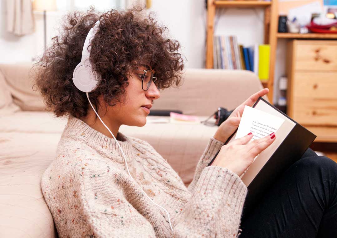 menina com fone de ouvido sentada no chão com um livro na mão