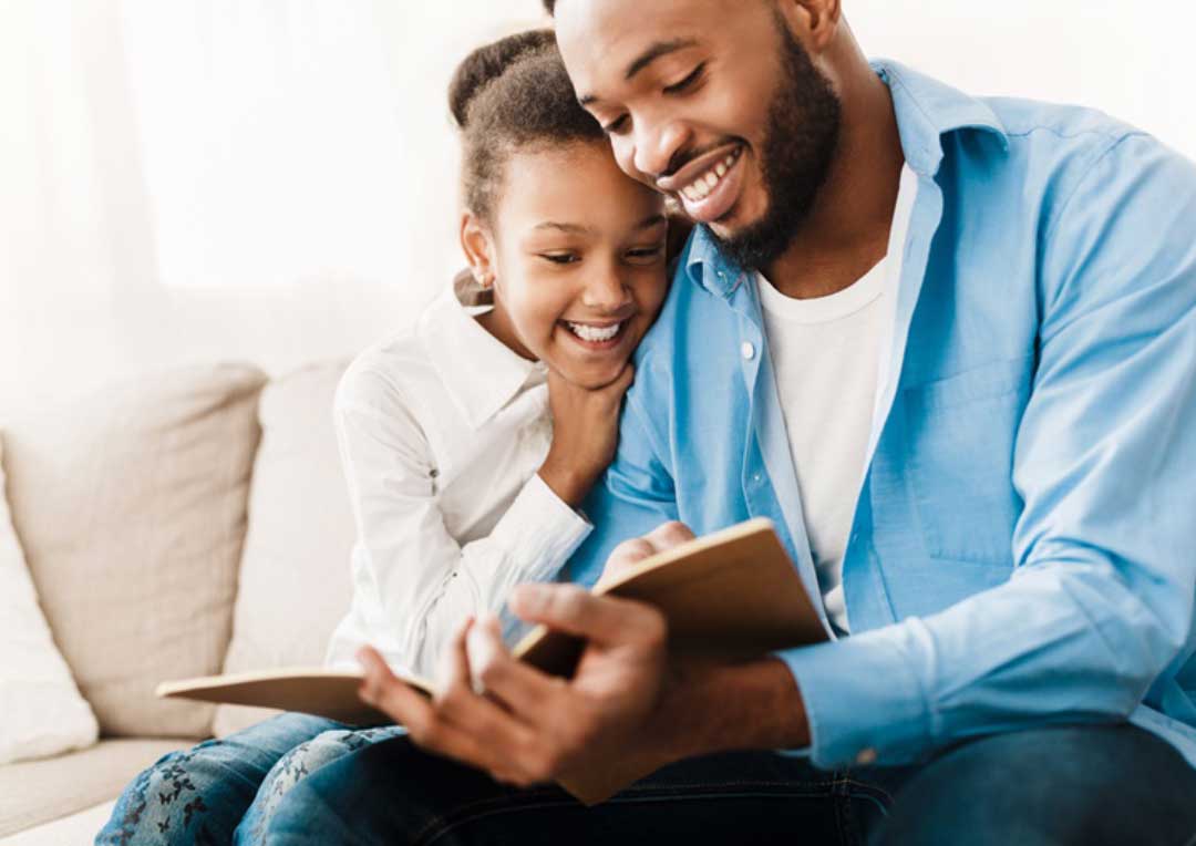 pai e filha sorrindo e lendo um livro juntos