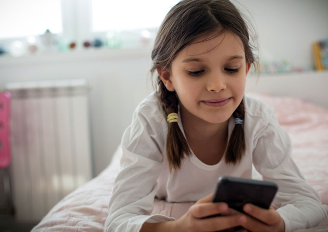 menina deitada na cama e segurando celular