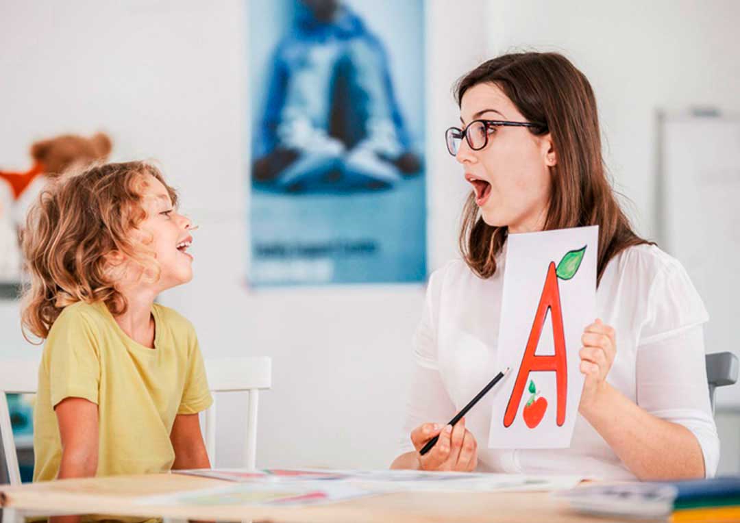 professora com uma cartaz com a letra e ensinando um aluno menino