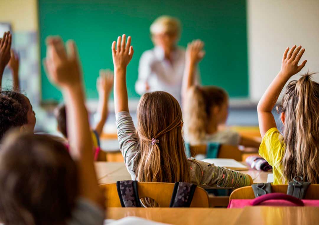 alunos na sala de aula com as mãos erguidas